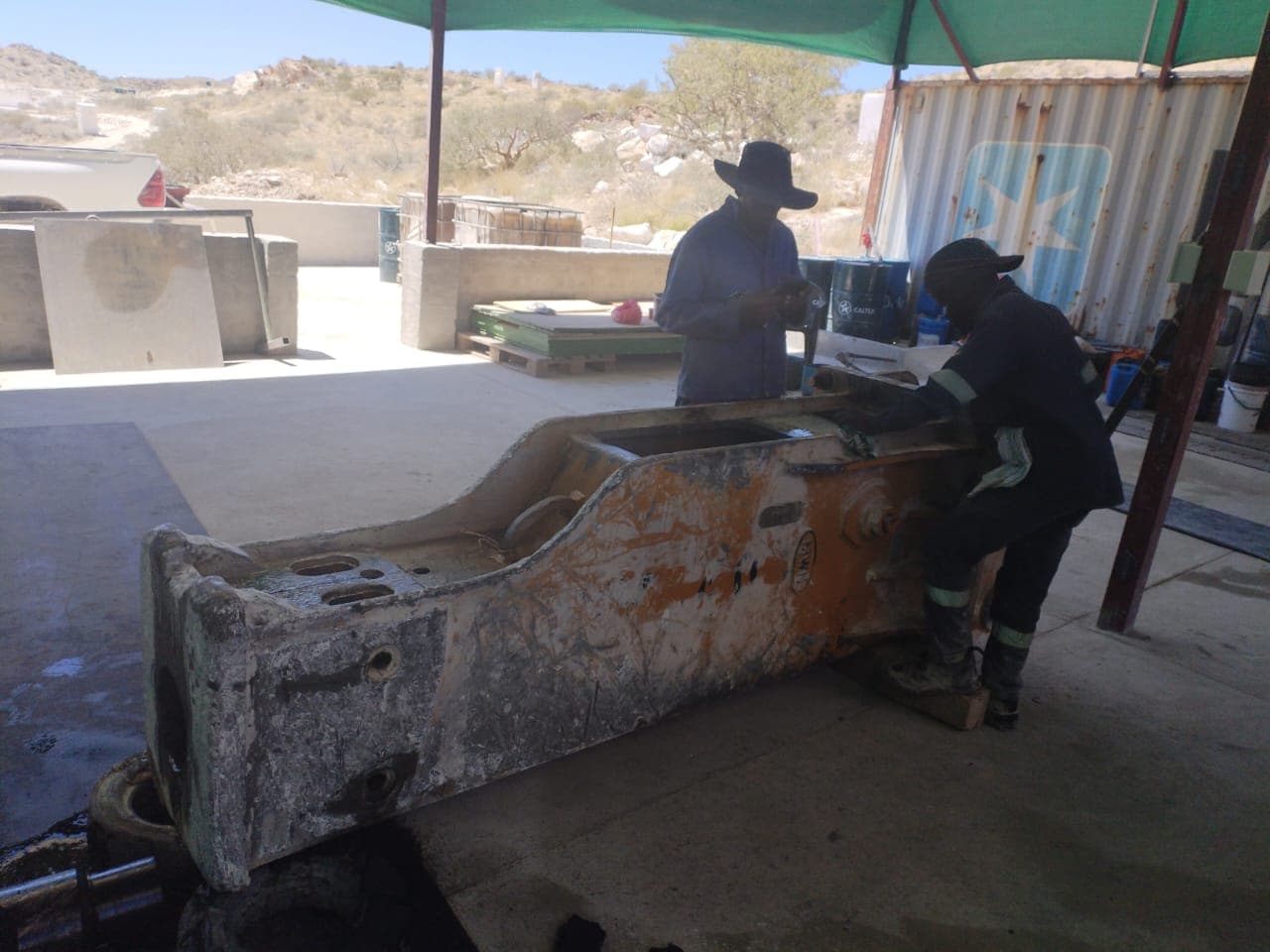 Technicians repairing a large hammer attachment inside the workshop area